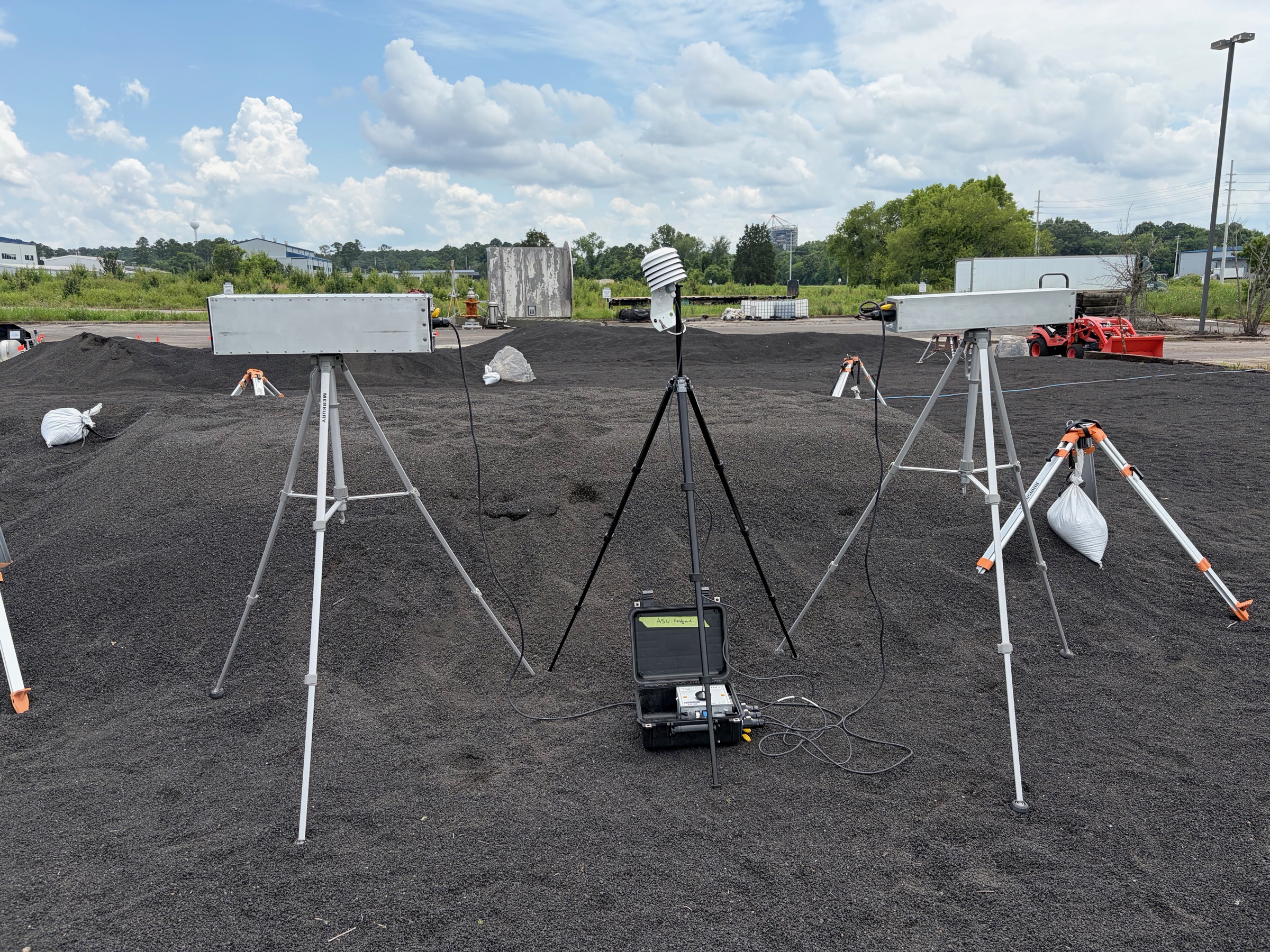 Two cosmic-ray neutron sensors on tripods flanking a weather station and data logger on dark regolith mounds at the NASA MSFC test field